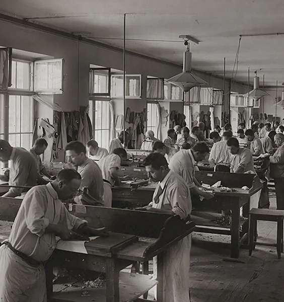 Historic black and white photograph of craftsmen working in a traditional workshop with wooden tables and tools